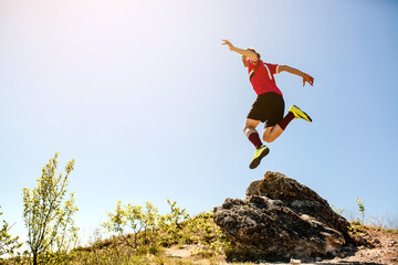 Young sportsman football player is jumping from the rock mountain