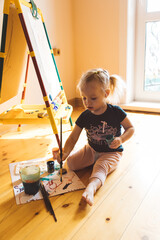 Obraz na płótnie Canvas Little girl sits on the floor and draws on an easel