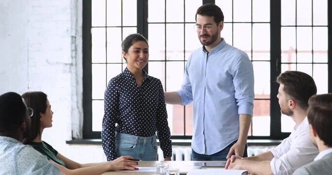 Friendly young business people welcoming new indian employee at workplace. Smiling confident male boss leader introducing happy female hindu newcomer to group of diverse teammates at first workday.