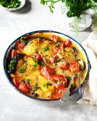 Baked fish (shark) with tomatoes and spices in a baking dish on a gray background, still life
