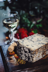 Piece of cheese with blue mold and a glass of white wine on a wooden board, selective focus. Cheese composition.