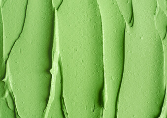 Green cosmetic clay (cucumber facial mask, avocado face cream, green tea matcha body wrap) texture close up, selective focus. Abstract background with brush strokes.