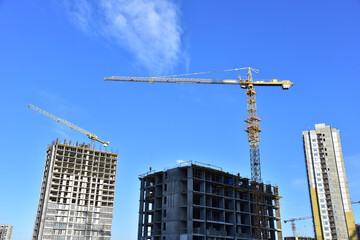 Tower cranes in action during construction residential building on blue sky background. Builder workers during formwork and pouring concrete. Crane lifting a concrete bucket and blocks