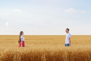 Fototapeta na wymiar Man and woman are standing in wheat field at distance from each other. People in field on sky background