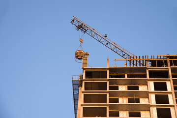 Naklejka premium Tower cranes working at construction site against blue sky. Crane lifting a concrete bucket. Construction process of the new residential buildings. Transportation blocks and pouring of the cement mix