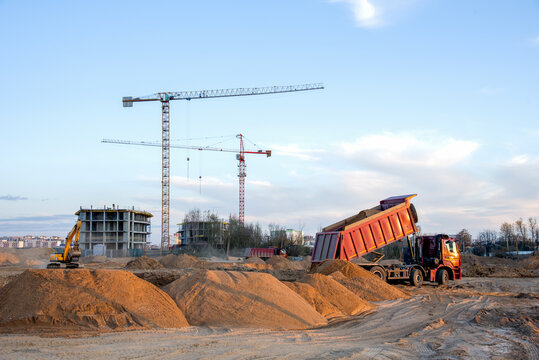 Dump truck unloading earth sand for road construction or for foundation work. Work of tower crane at construction site on blue sky background. Tall house renovation project, government programs