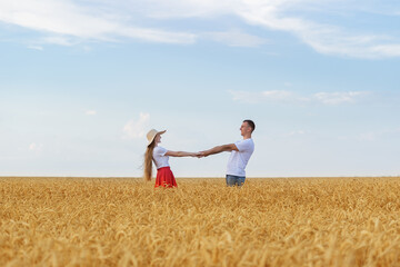 Young couple standing in middle of wheat field and holding hands. Romance of countryside