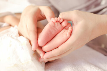 mother making heart sign hand in feet of newborn baby