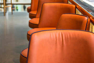 A row of empty orange leather upholstered swivel stools at a counter in a cafe