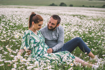 Couple in the flowers field and girl is a pregnant 