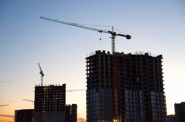 Fototapeta na wymiar Tower cranes in action at construction site on sunset background. Crane the build the high-rise building. New residential skyscraper. Tall house renovation project, government programs