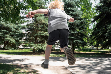 A little boy jumps far ahead in a park among the trees. View from the back