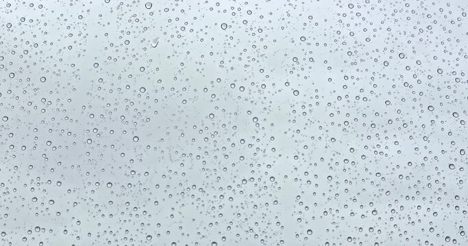 Macro view of abstract storm rain water drops falling down on window. Selective focus, dynamic zoom. Clouds on background.