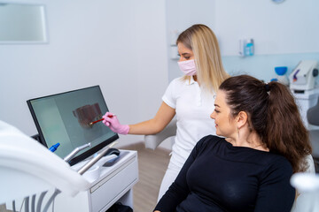 Dentist shows a patient x-ray of teeth on monitor. Explains methods of teeth treatment.
