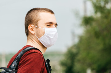 Side portrait of young caucasian male with white face mask and backpack looking to the side, empty...