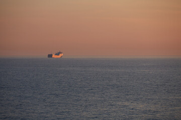 Commercial cargo ship sailing alone across North Sea in golden dusk light