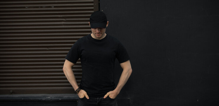 Man In Cap And Blank T-shirt Standing Against Black Wall