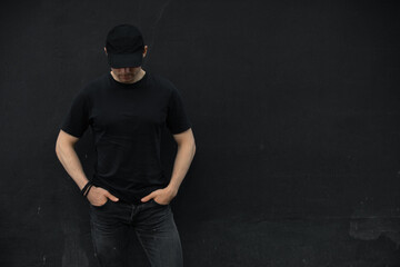 Man in cap and blank t-shirt standing against black wall - 353627260