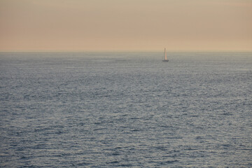 Obraz premium Sail boat sailing alone across vast sea in moody dusk light