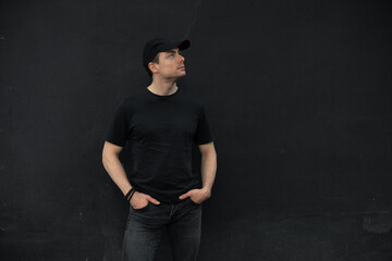 Stylish man in t-shirt standing leaning on black wall