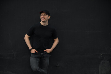 Stylish man in t-shirt standing leaning on black wall