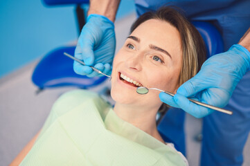 Dentist examining a patient's teeth using dental equipment in dentistry office. Stomatology and health care concept. Young handsome male doctor in disposable medical facial mask, smiling happy woman.