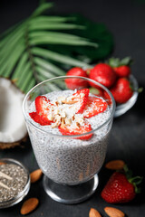Chia seeds pudding with strawberries and coconut chips in glass on dark background.