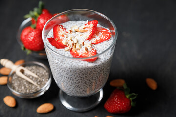 Chia seeds pudding with strawberries and coconut chips in glass on dark background.