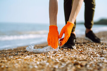 Men hand collects plastic bottle on sea beach. Volunteer wearing protective gloves collects bottle...