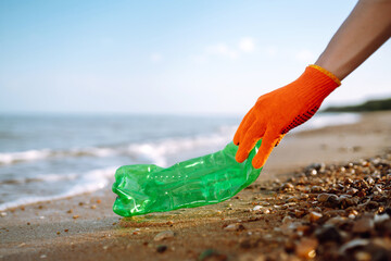 Men hand collects plastic bottle on sea beach. Volunteer wearing protective gloves collects bottle plastic. Seashore and water pollution concept. Environmental protection concept. 