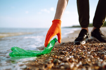 Men hand collects plastic bottle on sea beach. Volunteer wearing protective gloves collects bottle plastic. Seashore and water pollution concept. Environmental protection concept. 
