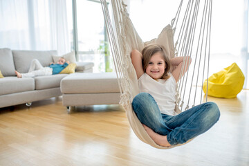 Adorable smiling girl enjoying on indoor swing in bright modern living room