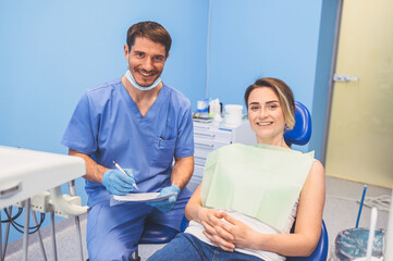 Dentist writes a conclusion and diagnosis in dentistry office. Stomatology and health care concept. Young handsome male doctor in disposable medical facial mask and gloves with smiling happy woman.