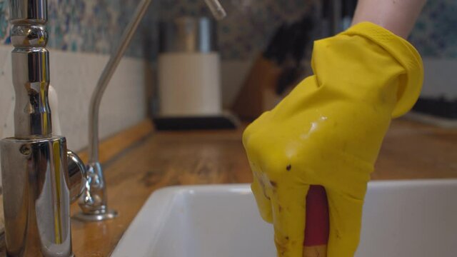Close up female hands in protective gloves cleaning a blockage in a kitchen sink with a plunger. Reparing of plumbing.