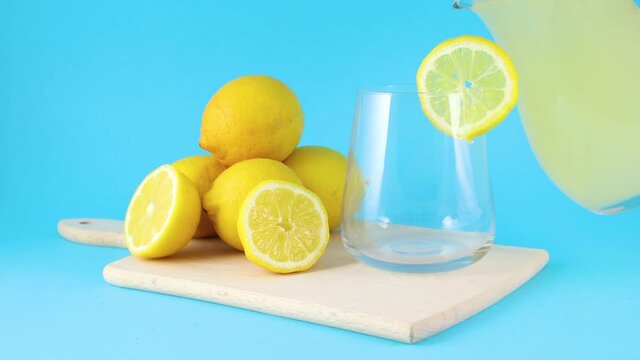 Pouring fresh squeezed lemonade form jug in drinking glass 