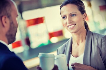 Portrait of businessman and businesswoman holding cup of coffee while talking and waiting for the train
