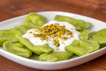 Close-up of traditional russian and ukrainian vegetarian green vareniki dumplings on a white plate, with sour cream and pistachios. Green dough colored with spinach juice. Ready to eat concept.