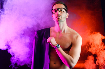 Athletic guy in a jacket shows his body on a bright background with smoke