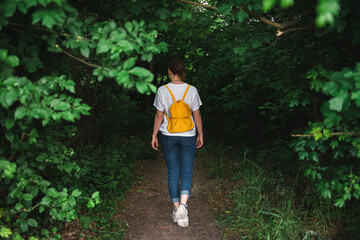 girl with a yellow backpack goes into a green dark forest