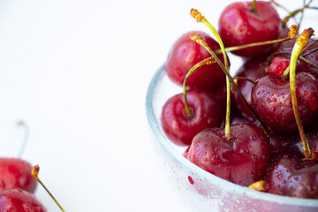 Ripe cherry berries with sprigs in a glass plate on a white background are located on the right edge of the image. Close-up.