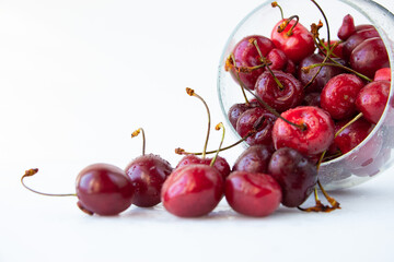 A bunch of ripe sweet cherry berries spills out of a glass goblet isolated on a white background. Close-up.