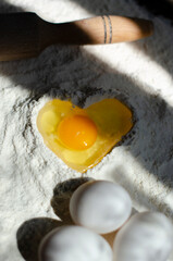 egg is broken into flour in the shape of a heart. cookie making process