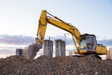 Excavator working at construction site on sunset background. Backhoe digs gravel and concrete...