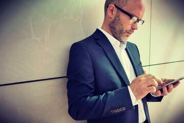 Portrait of businessman using smartphone while leaning on wall
