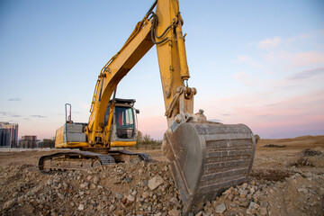 Excavator working at construction site on sunset background. Backhoe digs gravel and concrete...