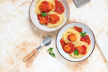 Italian spaghetti pasta with meat balls and tomato sauce served with oregano in two bowls on a light marble table. Top view, copy space