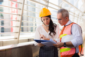 Elderly men and adult women wear formal dresses and protective hard hats. They carry documents and are talking. In the concept of a senior engineer or architect and advisor secretary