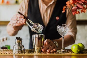 Male bartender putting a bg ice cube into a shaker while making daiquiri cocktail