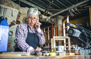 Senior female carpenter talking on the phone in her workshop