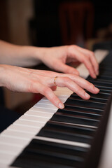 Fototapeta na wymiar Closeup of the hands of a young woman playing the piano. The girl musician is preparing to start playing a musical composition. Synthesizer or classical piano with classic keys. Music concept